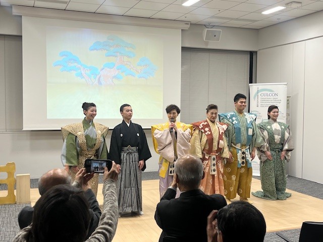JF本部の一室にて、6名の狂言師が来場席に向かって立っている。
