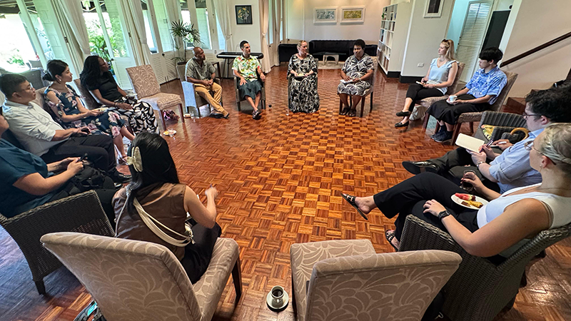 Twelve people are taking a commemorative photo in front of the Parliament of the Republic of Fiji.