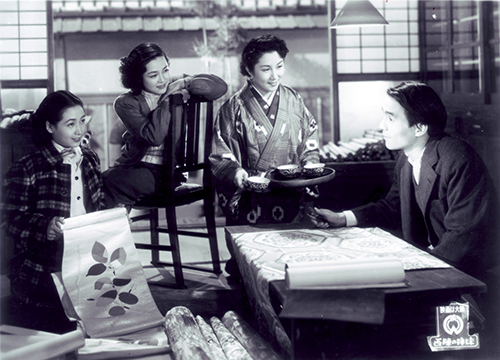A scene of three women and one man talking while looking at kimono fabrics and obis.