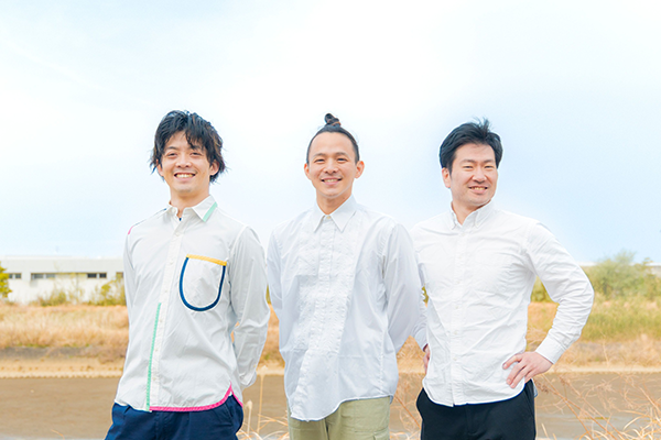 屋外で、Yシャツを着ているダンスカンパニー「んまつーポス」のメンバー3名。