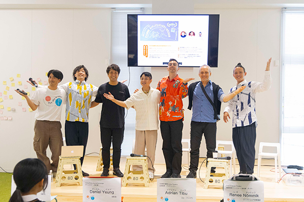 屋内のステージで、ディスカッション参加者である男性7名が写っている記念写真。