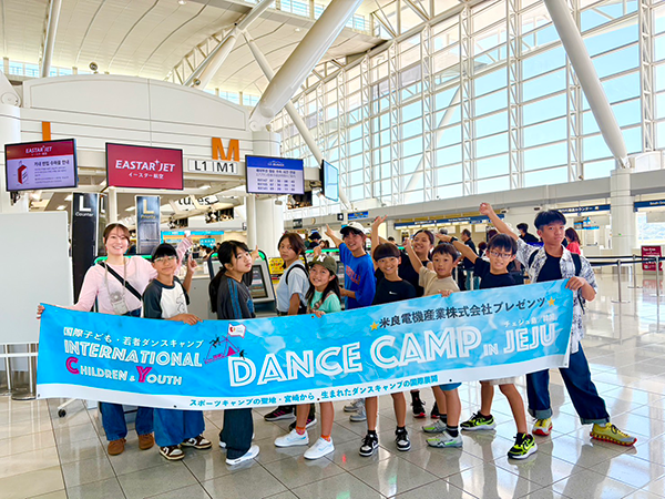 ステージにはオレンジ色のTシャツを着た国際子どもダンスキャンプ参加者約20名と、客席に観客数十名が座っている。