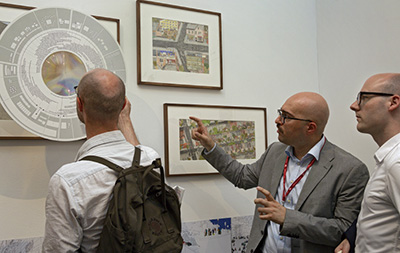 「第16回ヴェネチア・ビエンナーレ国際建築展」の展示を見ている3人の男性の写真