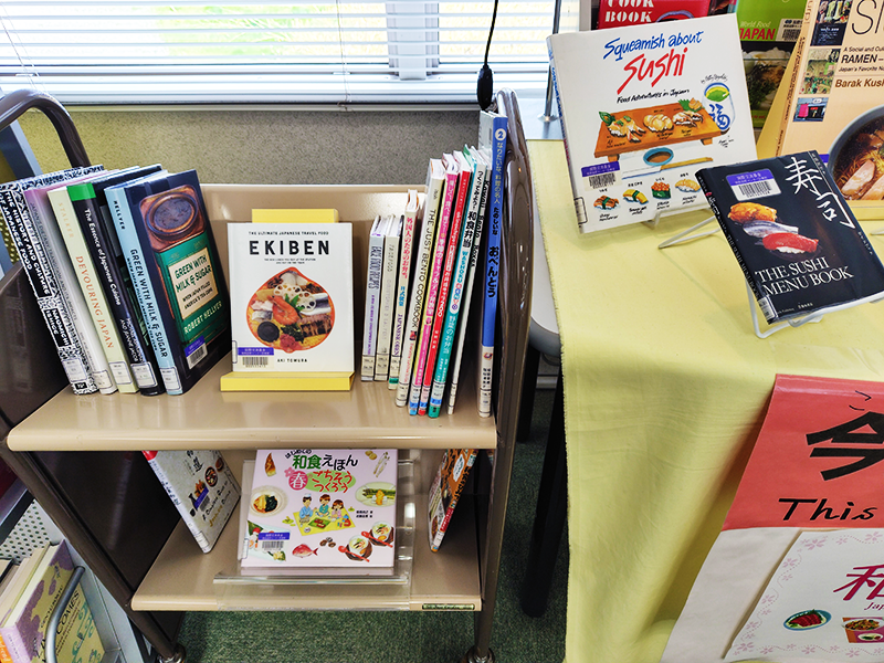 テーブルの横にある小さなラックに、4月の展示テーマである「和食」に関する本が約20冊並んでいる。