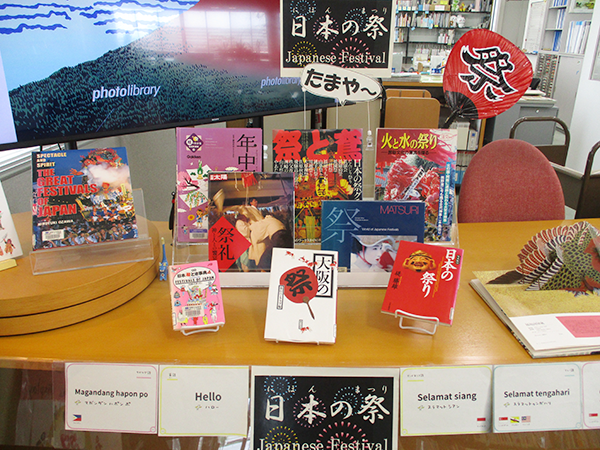 カウンターの上に日本の祭りに関する本が9冊が並べられ、その周りにポップやうちわがディスプレイされている。