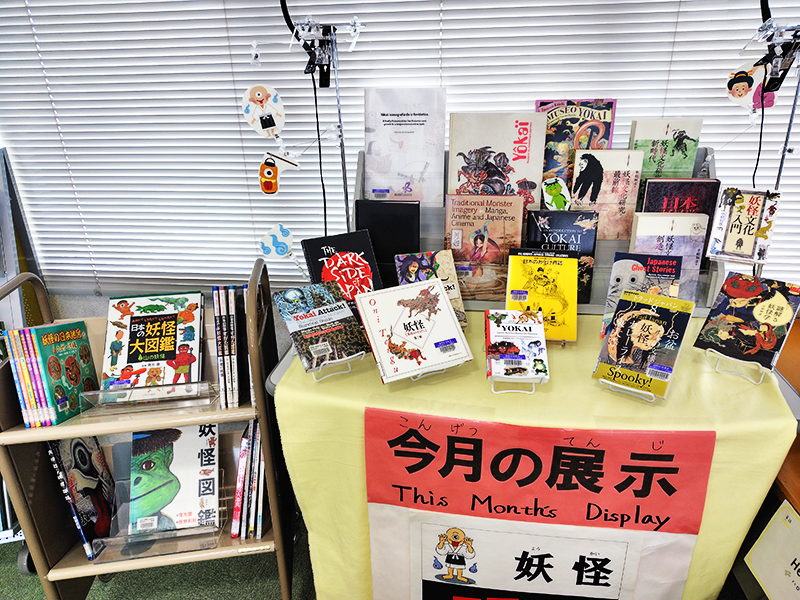 小さなテーブルの上に7月の展示テーマである「妖怪」の本が約20冊ある。テーブルの横にある小さなラックにも約15冊並んでいる。
