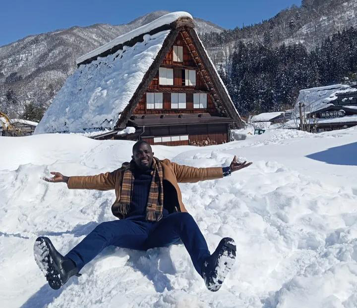 雪原が広がる白川郷の前で、雪の上に座るジャン・グザヴィエ・ウワンギ氏。