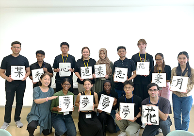 習字で漢字一文字が書かれた色紙を手に持って室内で2列で集合写真