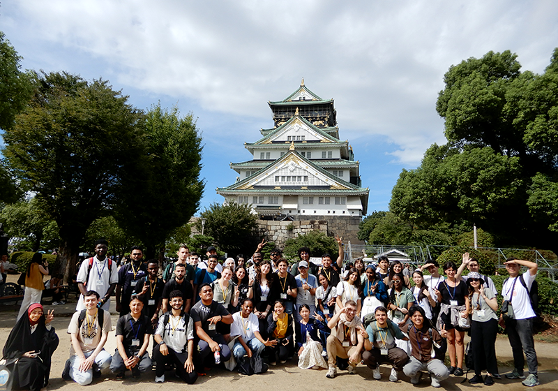 お城の前の気に囲まれたスペースで4~50名の参加者が記念撮影をしている