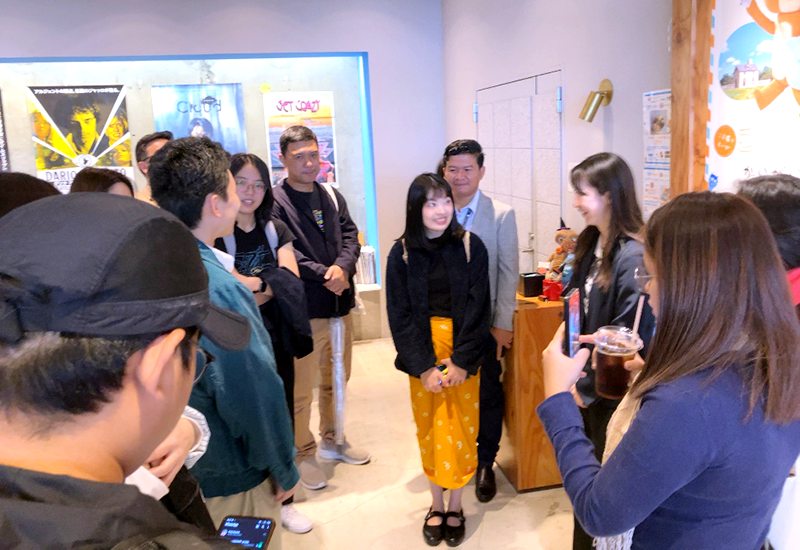 展示会場の展示物の前で一人の女性を囲んで10数人が談笑している