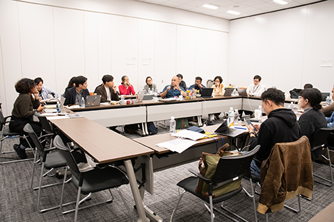 会議室で約16人が座ってディスカッションをしている。