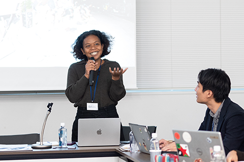 会議室のプロジェクターの前で女性1人がプレゼンをしている。