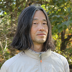 山下残氏のポートレート。屋外の木の前にいる。