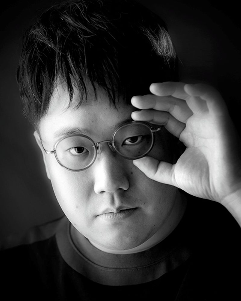 中澤陽のポートレート。かけているメガネの縁を持ちながらこちらを向いている白黒写真。
