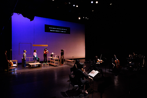 A view from diagonally left of the stage during a performance, with people playing instruments below the stage.