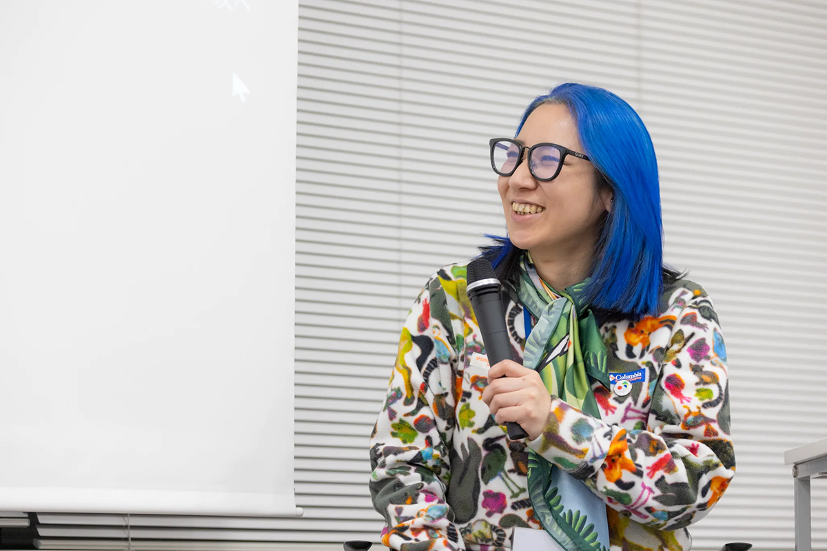 報告会の様子：マイクを持ち隣の登壇者の方を見るサエボーグ氏