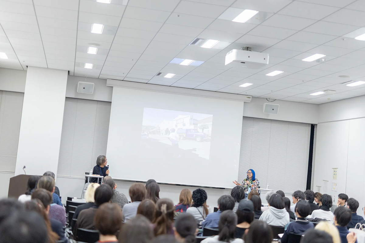 報告会の様子：会議室前方のスクリーンを挟んで発言する登壇者