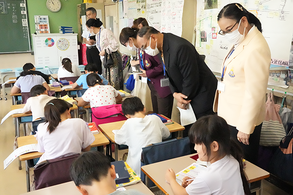 小平第八小学校の教室で小学生たちが机に向かって漢字ドリルをしている姿と、それを視察する参加者の6名。