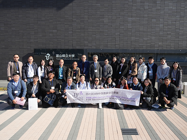 富山県立大学の校舎の前にて参加者27名が写っている