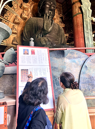 大仏を見上げながら説明パネルの解説を読む2名の人物の後ろ姿
