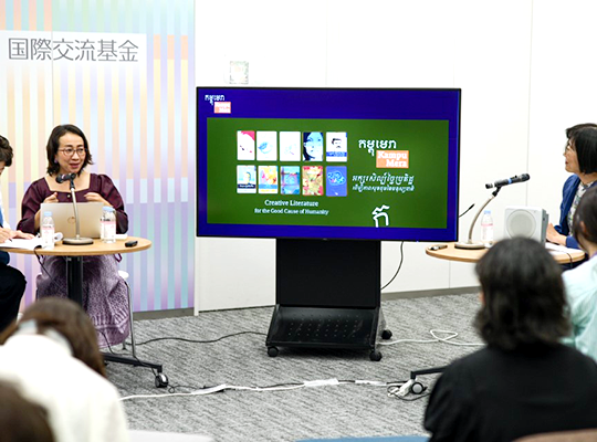 The speaker and participants are having a conversation across a display with a green screen.