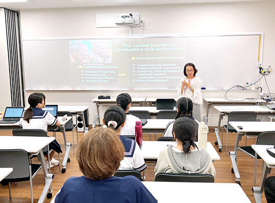 A woman lecturing to students in a classroom with white walls