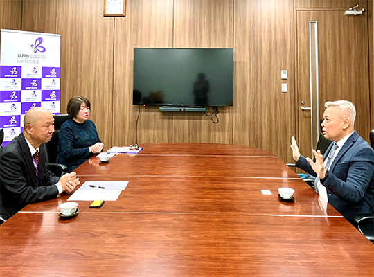 A man with his arms outstretched is talking across a desk with a JF director.