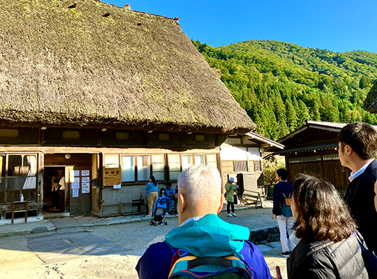 Several people are looking at a house with a thatched roof.