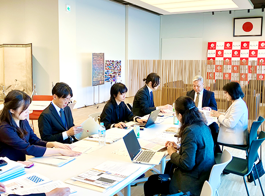 資A man listens to a staff member across a long table with food on it.