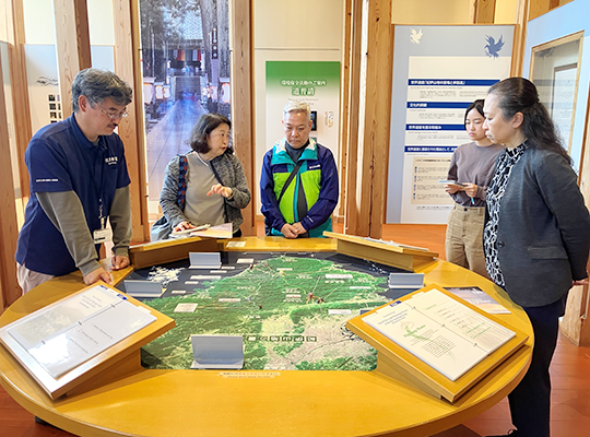 Men listening to a talk around a diorama set up at a round table