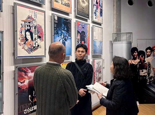 Director Pat Boonnitipat listening to Director Sasaki in front of a wall decorated with many exhibition panels