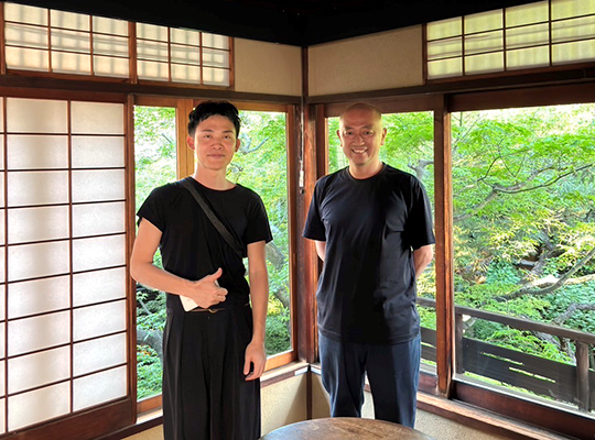 A photo of the two of them in a Japanese-style room with tatami and shoji screens with fresh greenery outside. On the left is director Pat Boonnitipat, and on the right is Shigenori Uotani.