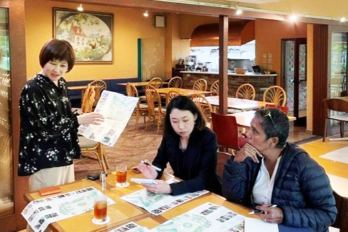 Three people, including Bella Galhos, are talking while spreading out a map on a restaurant table.