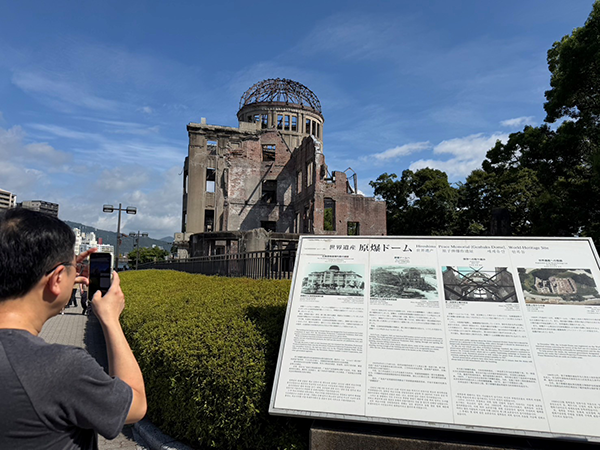 広島の原爆ドームを視察しスマートフォンでドームを撮影している。