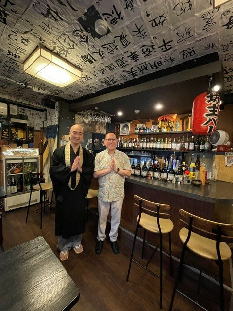 坊主バーで一般社団法人VOWZ代表理事の藤岡善信氏と手を合わせたポーズで記念撮影