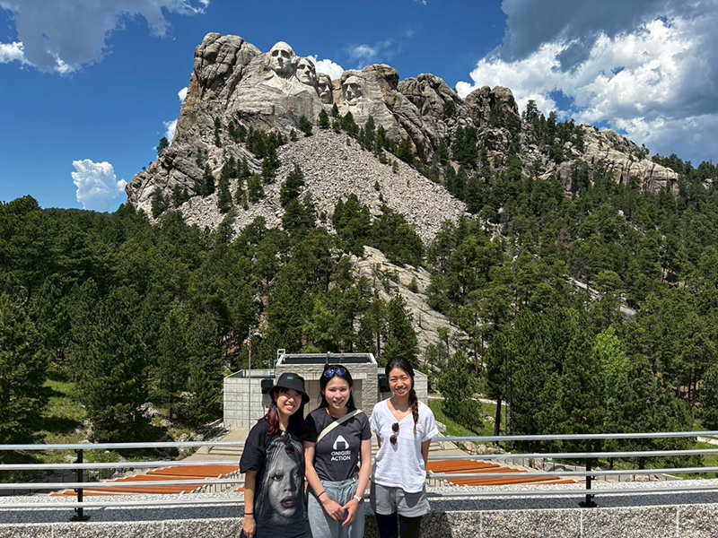 快晴のサウスダコタ州のマウント・ラシュモアを背景に女性3名が写っている。