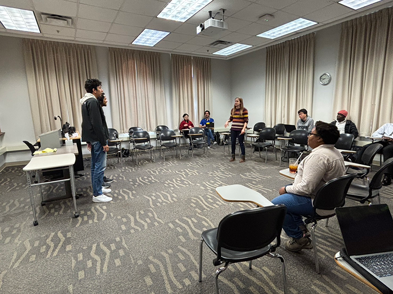 教室にて、3名が立ち上がり発言をしている様子を椅子に座っている6名が見ている。