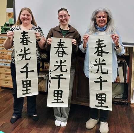3人の女性が「春光千里」と書いた書初めを持っている