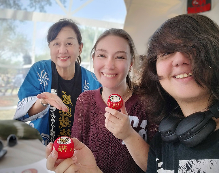2人の女性がそれぞれ製作した「だるま」を持っている。