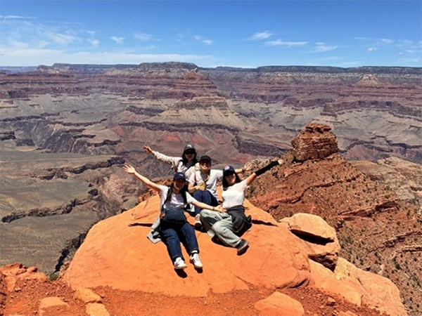 4人の女性がグランドキャニオンを背景に両手を上げて記念写真
