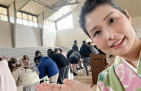 天窓から光の差し込む明るい広い体育館の一角で机にかがんで折り紙に打ち込む大勢の参加者と、それを笑顔で紹介している著者