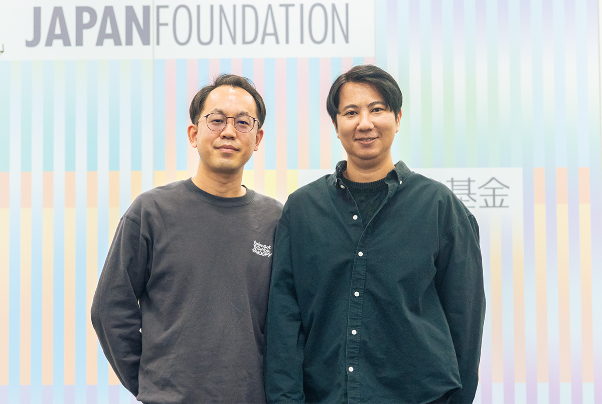 左に福冨氏、右にチラット氏が並んでJFの壁紙を前に記念撮影