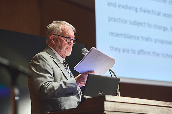 In the keynote speech of Part 1, Professor TUCKER is delivering his presentation next to the screen.