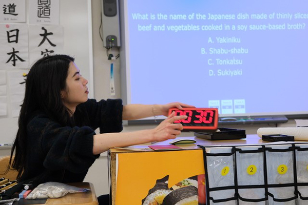 藪内志帆氏がデジタル時計を持ちながら日本語にまつわる知識を教えている様子の写真