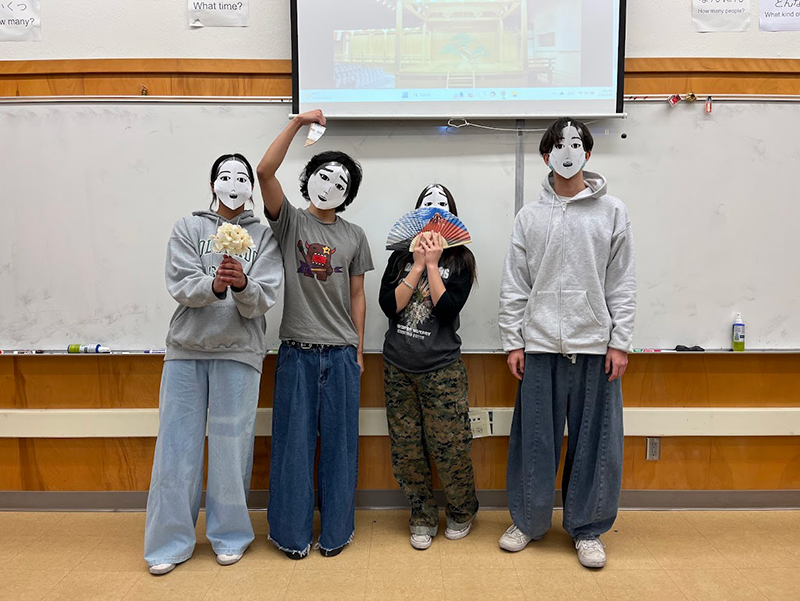 男女4人が手作りの紙のお面を被ってこちらを見ている。