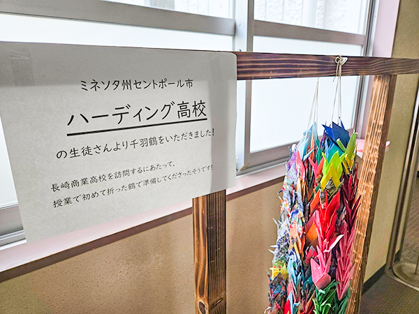 「ミネソタ州セントポール市ハーディング高校の生徒さんより千羽鶴をいただきました!長崎商業高校を訪問するにあたって、授業で初めて折った鶴で準備してくださったそうです!」という張り紙と千羽鶴が掲示されている。