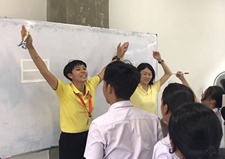 2人の教師が学生の前で両手を掲げてゲームの説明をしている様子の写真