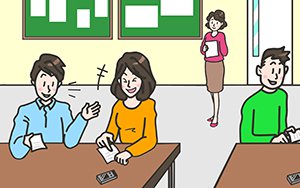 学習者がペアになってメモを手に楽しそうに話している様子。先生が後ろで学習者を見守っている。