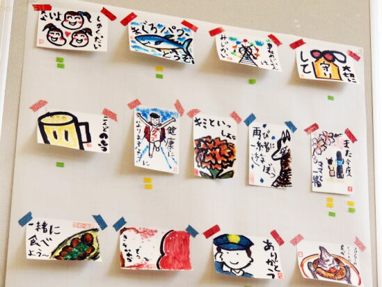 研修参加者がかいた、いろいろな絵手紙の作品がパーテーションにきれいに飾ってあるのを写した写真。絵手紙には、ケーキやたこやきなどの食べた物、桜やだるま、看板など町で目にした物、町で出会った人の絵などが描かれ、「一緒に食べよう」「君と一緒に」「ありがとう」などの短い文が添えられている。