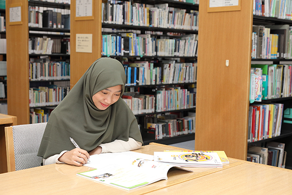 国際交流基金日本語国際センター図書館にて、ヒジャブを着ている女性1名が本を見ながらノートを書き取っている。